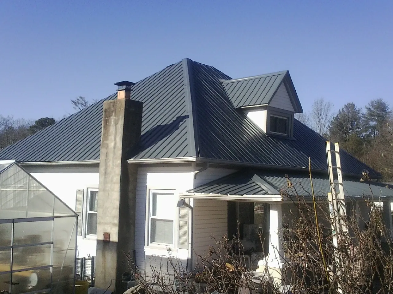 Dark blue standing seam metal roof on a white farmhouse with dormer — Slate & Tile Roof Repair by Roofing Brothers in Brogan