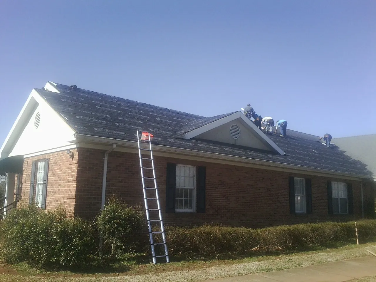 Crew tearing shingles off a brick ranch roof with a ladder set — Metal Roof Repair work by our crew in Brogan