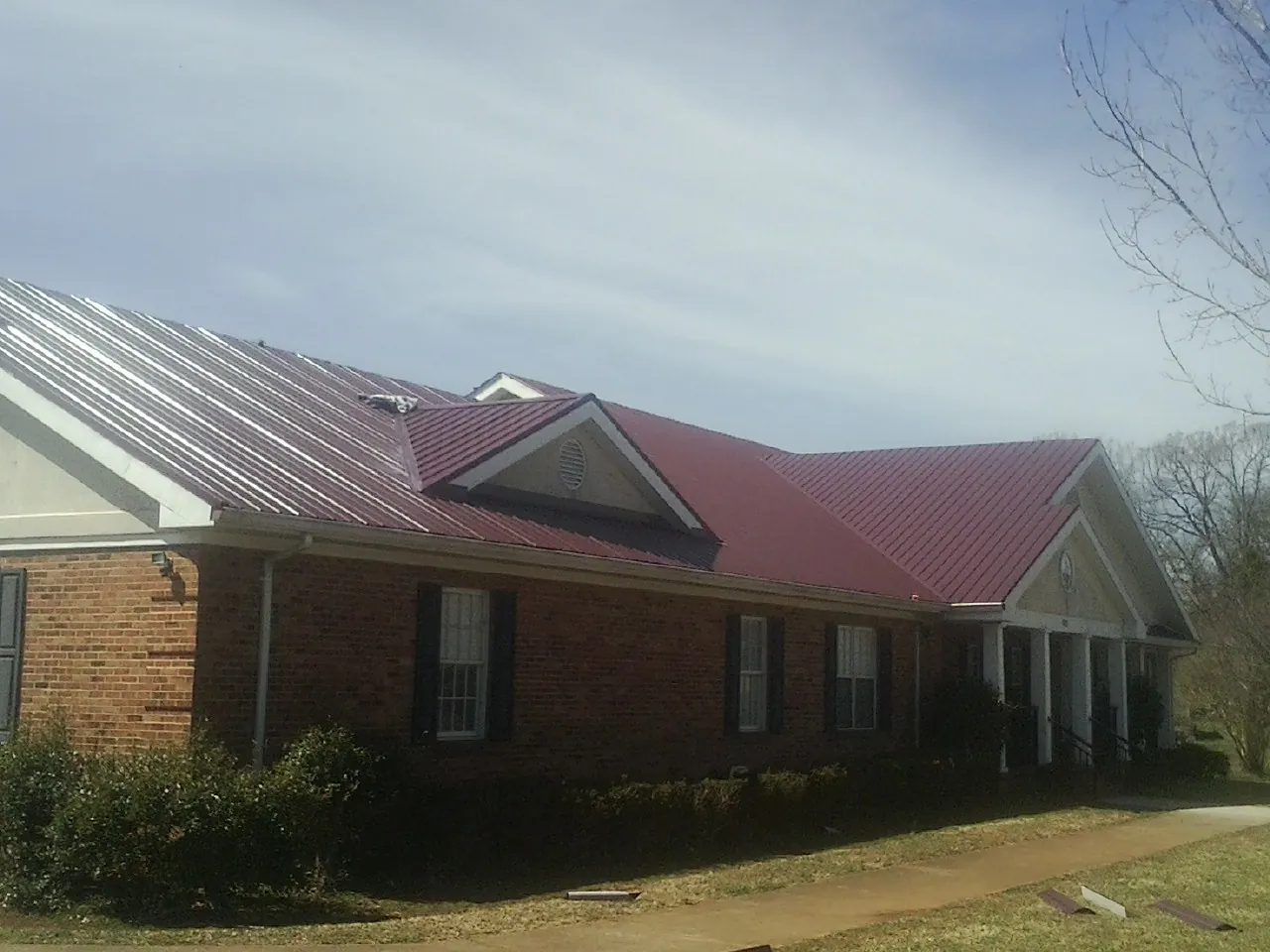 Red metal roof with gabled entries on a long brick building, from a Hail Damage Roof Repair job in Brogan