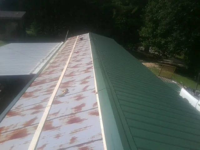 Old rusted panels beside newly installed green metal roofing — Wind Damage Roof Repair by Roofing Brothers in Brogan