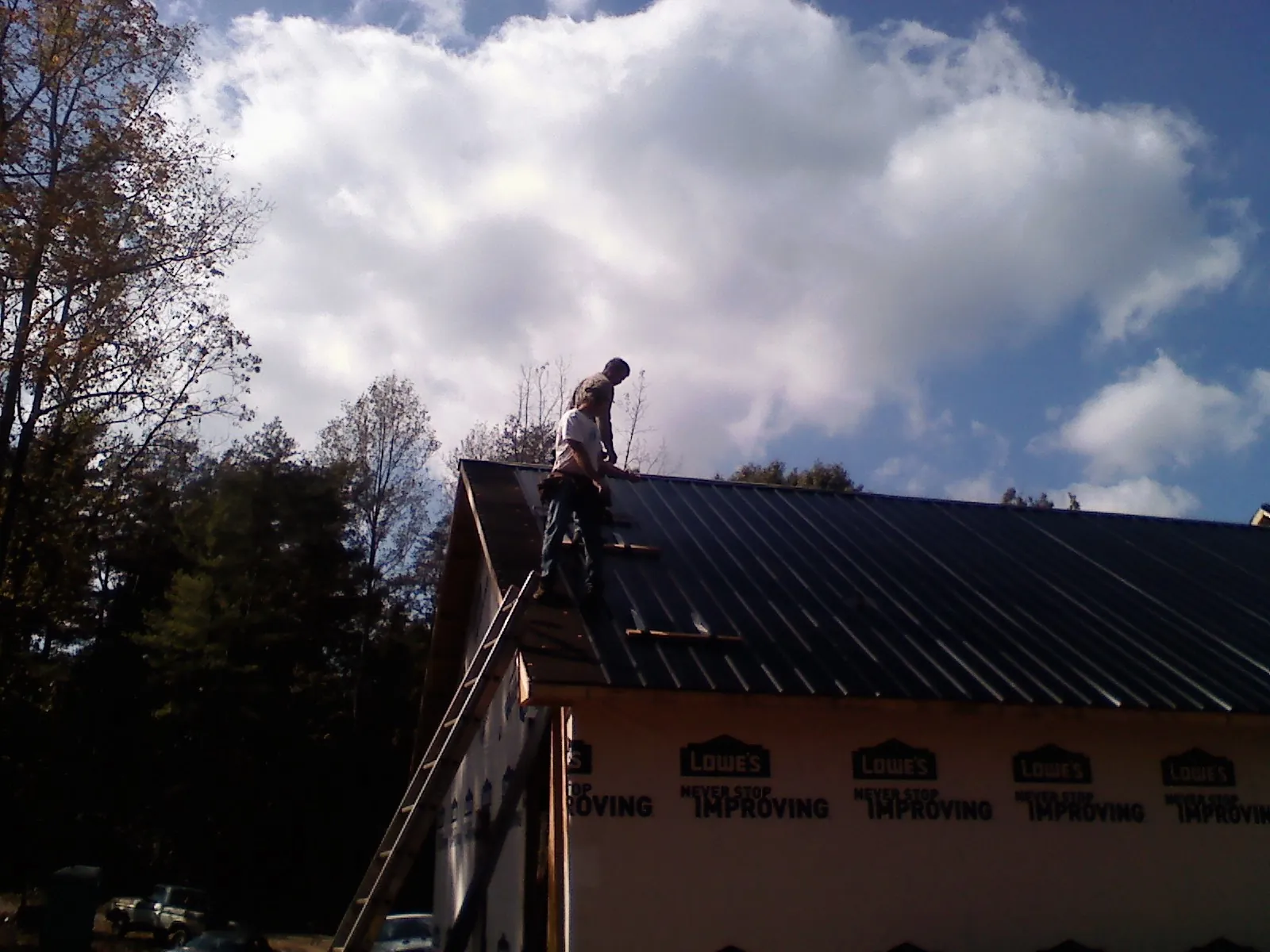Roofer fastening dark metal panels high against a cloudy sky, from a Roof Inspection job in Brogan