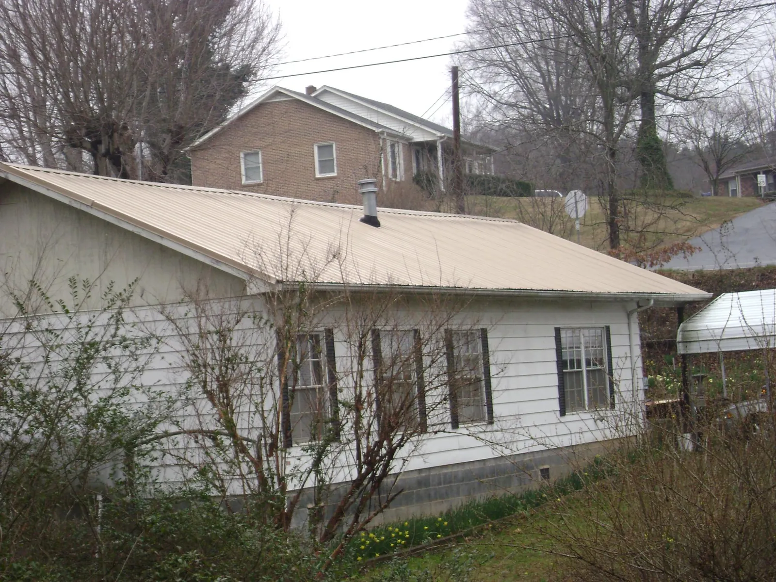 Tan metal roof on a white sided house set into a hillside — Commercial Roofing by Roofing Brothers in Brogan